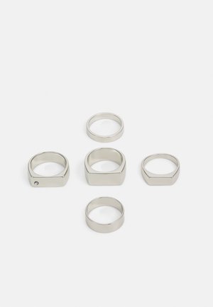 Set di sei anelli metallici argento in varie forme, tra cui rotondi e quadrati, caratterizzati da superfici lisce e un design minimalista.