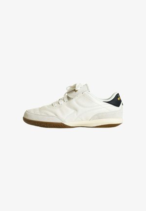 Sneaker bianca a taglio basso con suola color marrone chiaro, chiusura con lacci e linguetta del tallone nera con dettagli del logo dorati.