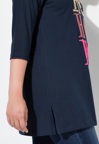 Marinblå t-shirt i mjuk bomull, med trekvartslånga ärmar, sidofickor och djärv text i rosa och guld på framsidan.