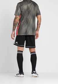 Harmaa ja musta raidallinen urheilu paita, jossa on punaisia yksityiskohtia, yhdistettynä mustiin shortseihin ja polvipituisii mustiin sukkiin, joissa on valkoiset raidat.