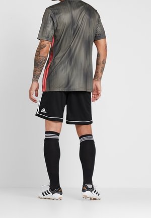Jersey atlético de rayas grises y negras con detalles en rojo, combinado con pantalones cortos negros y calcetas negras hasta la rodilla, con rayas blancas.