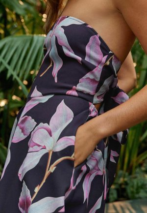 Rochie fără bretele cu un model floral închis, prezentând frunze mari de culoare roz și albastru. Materialul este neted, cu un design ajustat și un buzunar lateral ascuns.