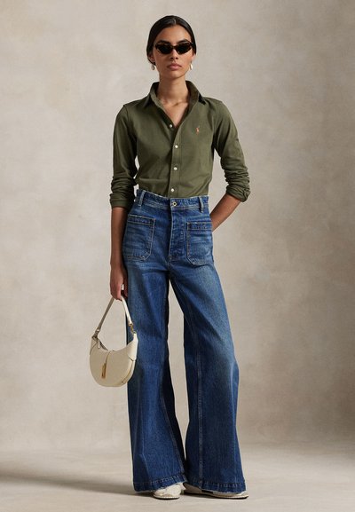 Olivovo zelená košeľa na gombíky, modré široké džínsové nohavice s vysokým pásom, biela kabelka, čierne slnečné okuliare; štruktúrovaná látka, veľké vrecká.