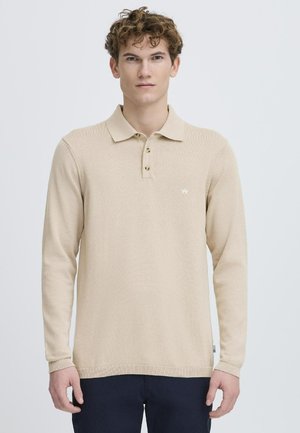 Camisa polo de manga larga beige con tres botones, cuello y puños acanalados, y un pequeño logo en el lado izquierdo del pecho. Tela suave y ligera.