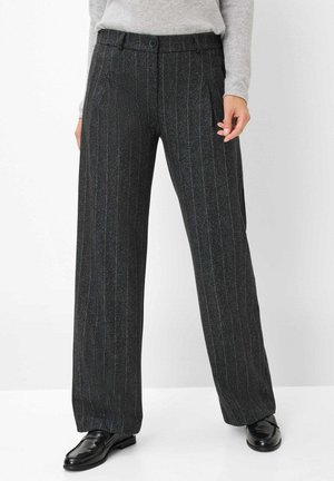 Woman wearing gray pinstripe wide-leg trousers, black leather shoes, and a light gray long-sleeve top, standing against a white background.