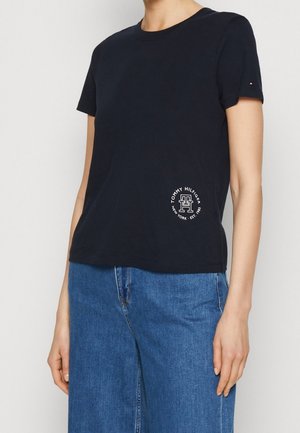 Ciemnogranatowy bawełniany T-shirt z okrągłym dekoltem, krótkimi rękawami i małym białym nadrukiem logo na dole po lewej stronie. Połączony z dżinsowymi spodniami.