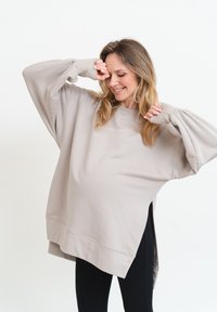 Beige oversized sweatshirt med rund halsringning, sidoflikar och långa ärmar, tillverkad av ett mjukt, strukturerat tyg. Broderad detalj fram.