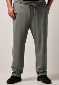 Grå sweatpants med elastisk talje og snoretræk, med sidelommer og et tapered ben design, parret med sorte sneakers.