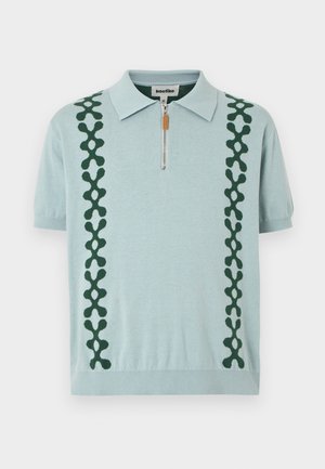 Polo de manga corta azul claro con patrón vertical de eslabones en verde, cierre frontal con cremallera y cuello de punto.