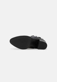 Suela de zapato negro con material de goma, superficie texturizada y tacón cuadrado. Incluye una ligera curvatura y un diseño de punta redondeada.