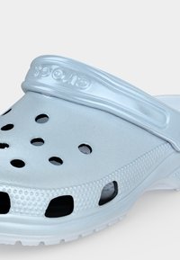 Sabot bleu clair à enfiler avec des trous de ventilation, des côtés texturés et une bride de talon réglable embossée du nom de la marque.