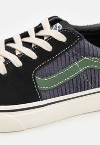 Black and gray corduroy sneaker with green leather accents, cream laces, and white sole. Features textured fabric and contrast stitching.