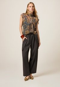Blusa de estampado floral transparente en tonos tierra, combinada con pantalones de pierna ancha oscuros, y finalizada con mules estampados y un brazalete ancho.