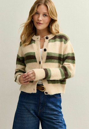 Crème cardigan met groene en bruine strepen, met een ronde hals, knoopsluitingen en ribgebreide mouwen, gecombineerd met blauwe denim jeans.