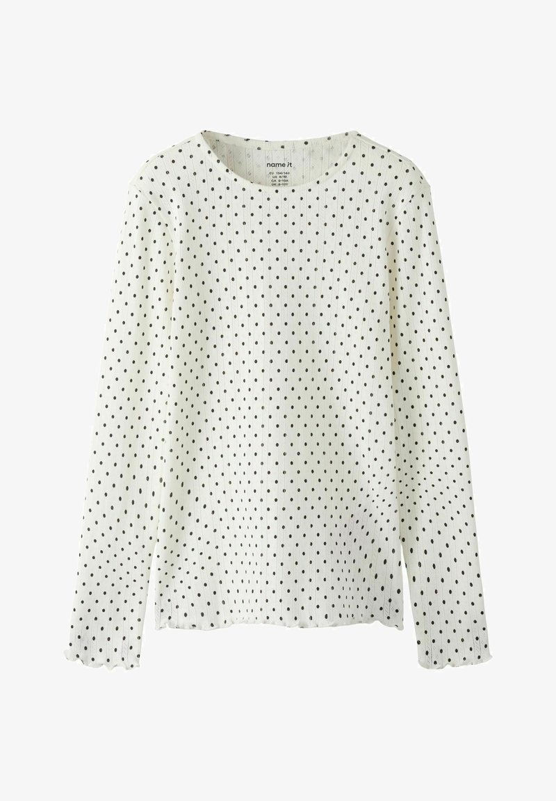 Hvid langærmet top lavet af struktureret stof med sorte polkaprikker. Har rund halsudskæring og bølgede manchetter. Enkel design.
