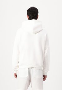 Sudadera blanca de algodón con capucha, mangas largas y un corte relajado, complementada por una textura suave y un dobladillo acanalado.
