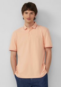 Pfirsichfarbendes Polo-Shirt mit zwei Knöpfen, geripptem Kragen und Bündchen, versehen mit burgunderfarbenen Akzenten, aus hochwertigem, glattem Baumwollgemisch.