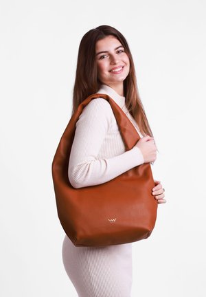 Braune Ledertasche im Hobo-Stil mit glatter Textur, breitem Träger und dezentem Logo-Detail, gehalten von einem Modell, das ein helles, geripptes Kleid trägt.