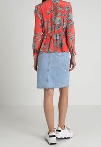 Czerwony kwiatowy top z długimi rękawami, wcięty w talii, zestawiony z wyblakłą niebieską spódnicą dżinsową z surowym wykończeniem i białymi sneakersami.