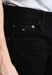 Czarne jeansy z denimu z przednią kieszenią ozdobioną metalowymi ćwiekami oraz małym haftowanym logo w kolorach czerwonym, białym i niebieskim.