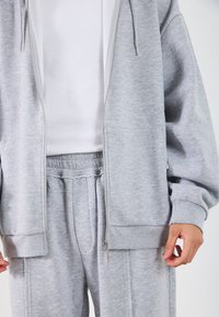 Heledhall hallide pitsaga, millel on känguru-taskud, ribitud varrukad ja täielikud varrukad, koos sobivate trenni pükstega, millel on elastne vöökoht.