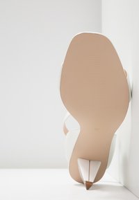 Bílé sandály na vysokém podpatku s páskami, špičatou špičkou a malým stiletto podpatkem. Texturovaná světle béžová podrážka. Velikost 37 označena na podrážce.