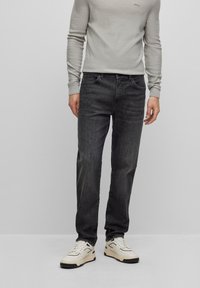 Mörkgrå jeans med rak passform, gjorda av denim, kombinerade med en ljusgrå figursydd tröja, bärs med vita sneakers.