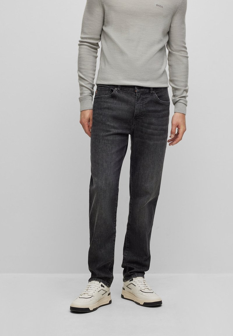 Mörkgrå jeans med rak passform, gjorda av denim, kombinerade med en ljusgrå figursydd tröja, bärs med vita sneakers.