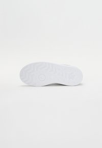 Fehér sneaker talp, texturált cikkcakk mintával, kör alakú és kiemelkedő díszítőelemekkel, valamint apró lefolyónyílásokkal a jobb tapadás és rugalmasság érdekében.