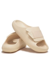 Beige slipper sandalen van flexibel materiaal, met een open teen, gevoerde voetbed en een stofband over de bovenkant.