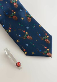 Marineblauer Krawatte mit Rentiergesichtern, die festliche Brillen und Ornamente tragen, begleitet von einer silbernen Krawattennadel mit einem roten, kreisförmigen Akzent.