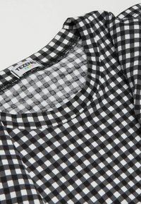 Czarny i biały t-shirt w kratkę z okrągłym dekoltem i krótkimi rękawami. Materiał jest miękki o gładkiej fakturze. Widoczna metka marki.