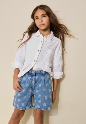 Biela košeľa na zapínanie so štruktúrovanou látkou, v kombinácii s modrými rifľovými šortkami s veľkými svetlomodrými bodkami. Jednoduchý dizajn a voľný strih.