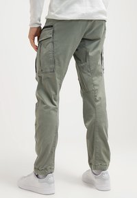 Ljusgröna cargo-byxor i bomull, med sidofickor, elastiska mudd, och en avslappnad passform, i kombination med vita sneakers.