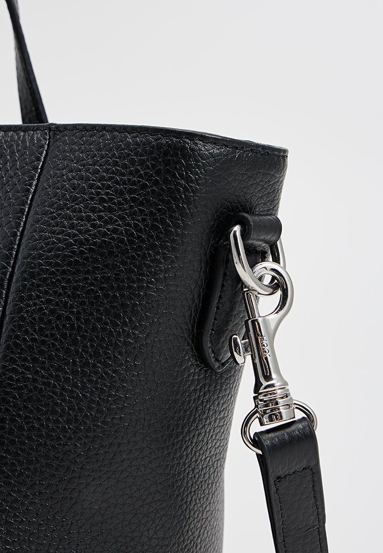 Nahaufnahme einer schwarzen strukturierten Lederhandtasche mit glänzendem silbernem Metallverschluss, der den Gurt mit der Tasche verbindet.