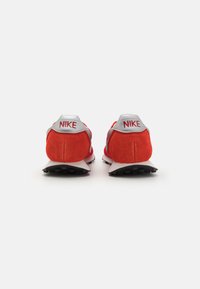 Crvene nubuck tenisice s mrežastim dijelovima i crnim gumenim potplatom, s srebrnim detaljem na peti i "NIKE" logotipom u crvenoj boji na petama.