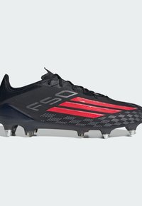 Μαύρο ποδοσφαιρικό παπούτσι με κόκκινες ρίγες, σχέδιο με κορδόνια και μεταλλικά καρφιά στη σόλα για πρόσφυση σε χλοοτάπητες.