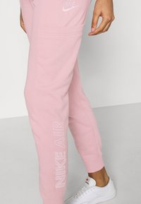 Ljust rosa Nike Air sweatpants med sidoficka, med en texturerad vit logotyp längs benet och mjukt, bekvämt tyg.