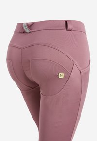 Leggings aderenti a vita alta in morbido tessuto mauve. Presentano cuciture decorative, tasche posteriori curve e un piccolo etichetta con logo.