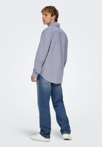 Lyseblå skjorte med krave og afslappet pasform, med knapmanchetter og en let buet kant, kombineret med slidte blå jeans og hvide sneakers.