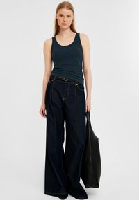 Dunkelblaue Tanktop kombiniert mit weit geschnittenen, dunklen Denim-Jeans. Das Outfit wird durch eine schwarze Lederhandtasche ergänzt.