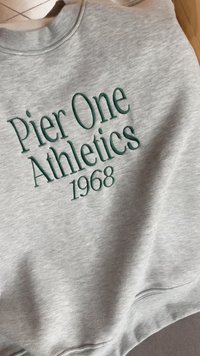 Šedá mikina s potiskem zeleným vyšívaným textem, který zní "Pier One Athletics 1968." Hladká látka s designem kulatého výstřihu a pružnými manžetami.