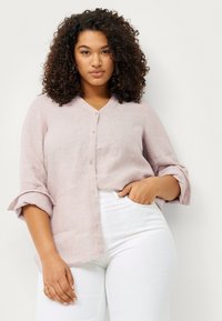 Light pink, linen button-up shirt with a V-neck, rolled sleeves, and a relaxed fit. Paired with white jeans. Natural texture visible.