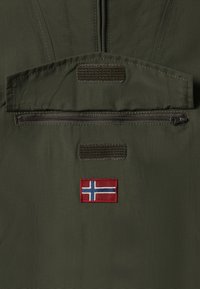 Grön tyg med en slät yta har en ficka med dragkedja och en kardborreflik. En broderad norsk flagga syns tydligt.