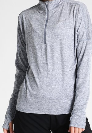 Persoon draagt een lange mouw grijs gemêleerde sportpullover met een korte rits bij de hals en zwarte broek.