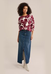 Sarkans ziedu raksts džemperis ar garām piedurknēm, apvienots ar augstās jostasvietas denima maxi svārkiem ar priekšējo šķēlumu un baltām zābakiem līdz potītēm.