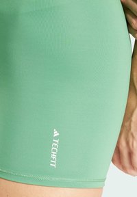 Gröna sportshorts gjorda av mjukt, stretchigt material. Har en vit "TECHFIT"-logotyp och en åtsittande design som når mitt på låret.