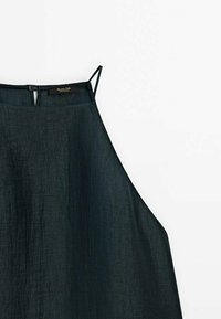 Haut sans manches vert foncé avec des bretelles fines, présentant un tissu léger et texturé ainsi qu'une fermeture à boutons à l'arrière du col.