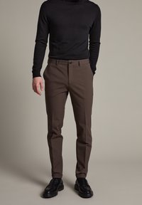 Mörkbruna skräddarsydda byxor med slät yta, med knappstängning och framfickor, kombinerat med en åtsittande svart tröja.