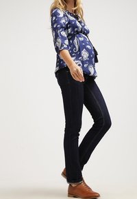 Tyrkysová blůza s paisley vzorem a tříčtvrtečními rukávy, doplněná tmavými skinny džíny a hnědými koženými šněrovacími botami.